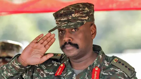 Getty Images Gen Muhoozi Kainerugaba salutes at a military drill competition. He is wearing military fatigues - his epaulettes show he is a four-star general