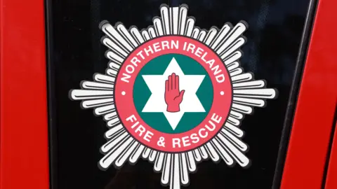 NIFRS logo, which is white and black and says Northern Ireland Fire and Rescue Service with a red hand of ulster in in the centre of a white star.
