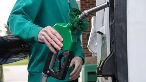 A man in a green jumper returns a petrol pump after refilling his car