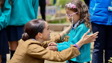 Reuters Meghan reaches to embrace a young girl wearing glasses during a visit to a local public school at Las Cruces neighborhood, in Santa Fe, Colombia on August 16