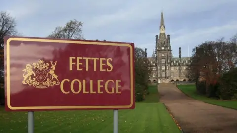 A sign in the foreground says Fettes College. In the background is the stone built school.