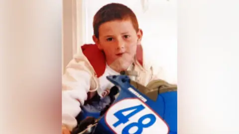 Supplied A photograph of Anthony Binfield as a child, wearing a white hoody with a red lining on a toy motorbike with the number '48' on the front.