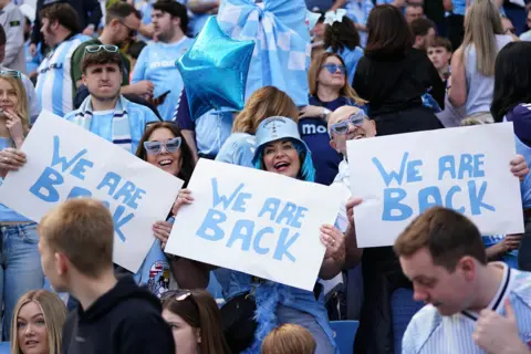 PA Media Three Coventry City fans in a crowd hold up signs which say "We are back"