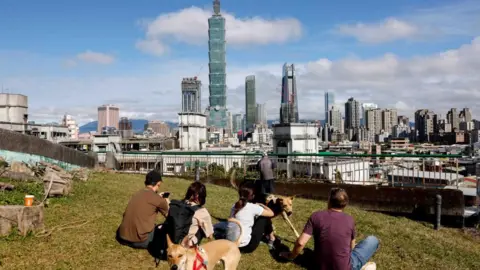 Reuters People look at the building while sitting on a patch of grass from a distance 