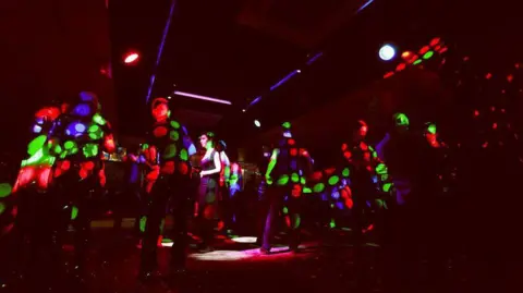 The Willow Community Digital Archive/Ceri Oakes Photography Dancers in a dark nightclub, with red, green and blue lights shining on them.