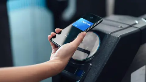 Woman taps mobile phone on TfL ticket barrier