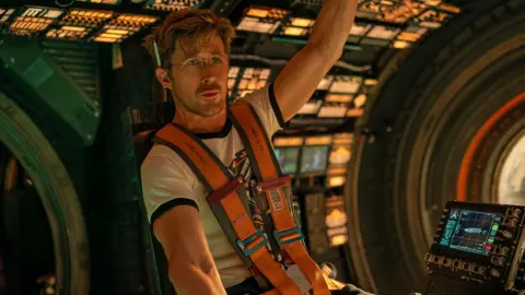 Sony Pictures Ryan Gosling in a promotional still for the film is strapped in to a space pod wearing glasses and a pencil behind his ear and looking pensive.