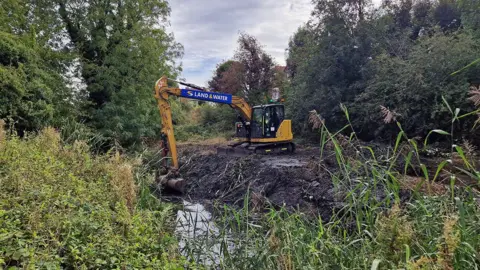 Rushcliffe Borough Council A yellow digger amongst the greenery of a nature reserve digging out silt from a waterway