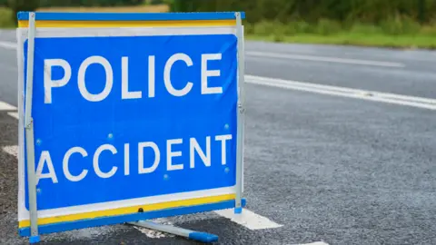 A blue and white sign reading Police Accident is erected at the side of a main road