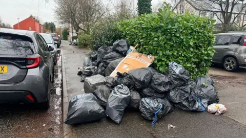 Gabriel Bononi A pile of black bin bags in the middle of the pavement blocking the passage.