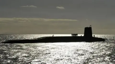 PA Media A wide shot of a submarine at water level. The sun has gone down and is glistening on the sea.