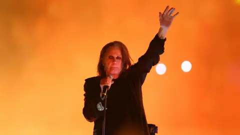 Reuters A photo of a man wearing all black. He is holding a microphone. His eyes have got black eyeliner around them. He has long brown hair. 
