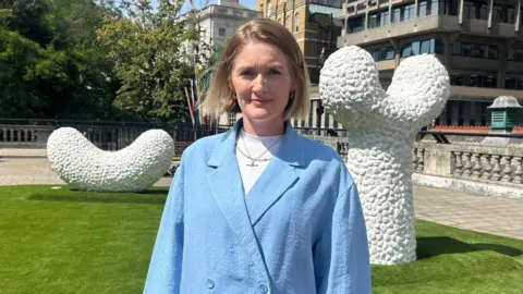 Alice Walters in a blue blazer standing front of a white sculptures.