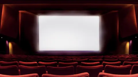 A blank cinema screen with rows of red chairs in the foreground