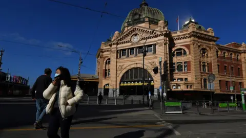 EPA Person wearing a mask walks past a deserted Flinders Street Station