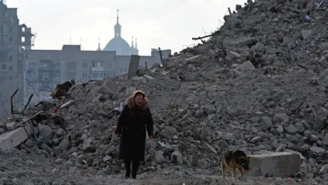 Reuters A woman and a dog walk in the rubble of Mariupol