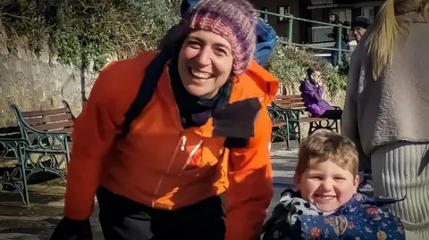 Family photo Sarah and Ivor are walking on a city street. Both are looking at the camera and smiling. They both have on winter coats
