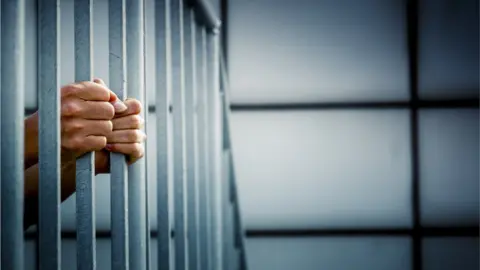 Getty Images Hands holding prison bars