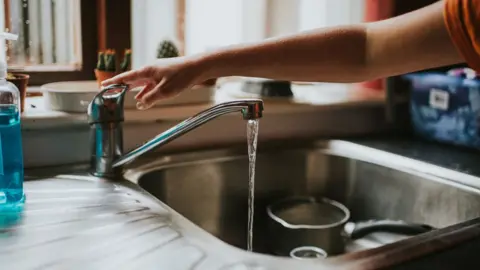 Getty Images Hand turning off a Running Chrome Tap in a kitchen - stock photo