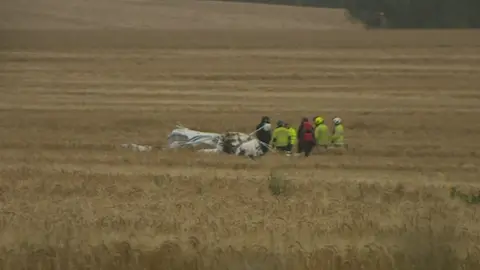 BBC The crash plane in the field with emergency personnel around it