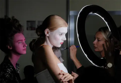 Sergey Dolzhenko / EPA Models stand and wait as they have full-face make-up applied by a make-up artist