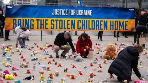 Thierry Monasse/Getty images People light candles beside teddy bear in Brussels, on February 24, 2023