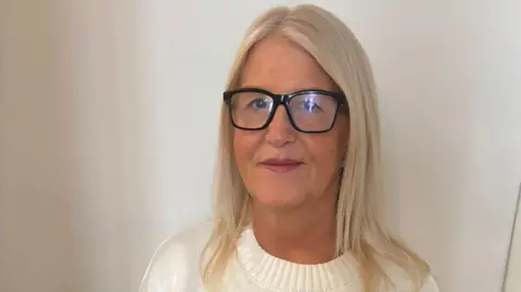 Carol Boon Carol Boon, a woman with shoulder-length blonde hair and black-rimmed glasses. She is smiling while standing in front of a white wall and wearing a white jumper. 