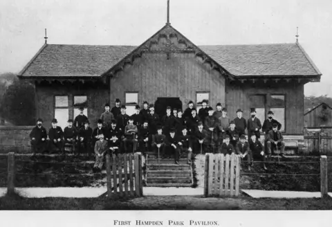 A black and white photograph with a lot of men in hats and dark suits posing for a photograph