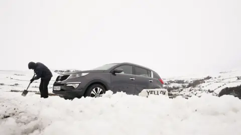 PA Media A man digs out a car in heavy snow in the Yorkshire Dales