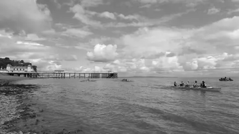 Tracey Dunford Rowers in the sea off Penarth, with the pier in the background - a black and white image