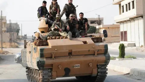 Reuters Turkish-backed Syrian rebel fighters sit on an armoured vehicle in Tal Abyad, Syria (21 October 2019)