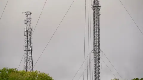 Martin Giles/BBC Tacolneston transmitter: two grey metal tower structures - with a grey cloudy sky in the background