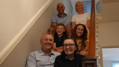 Bill and Jo sit on stairs with two children and two adults