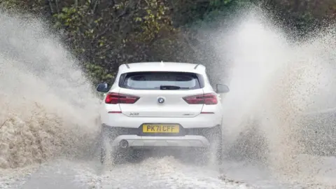 PA Media A car driving through floodwater