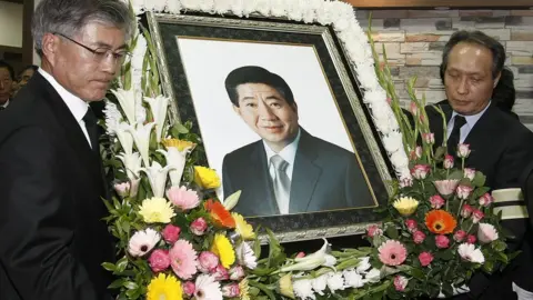 Getty Images Memorial for former Roh Moo-hyun at his service. Photograph surrounded by flowers.