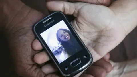 Caritas Dr María Alarcóm holds a phone with a photo of her daughter on it