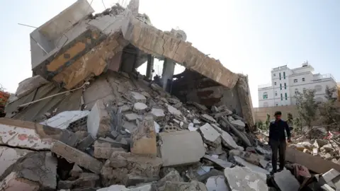 EPA A man walks through the remains of a building destroyed in a Saudi-led coalition air strike in rebel-held Sanaa, Yemen (7 October 2021)