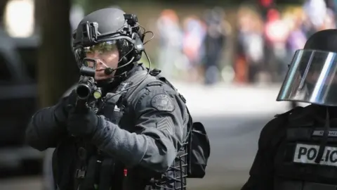 Getty Images A police officer shoots non-lethal rounds at demonstrators in Portland (04 June 2017)