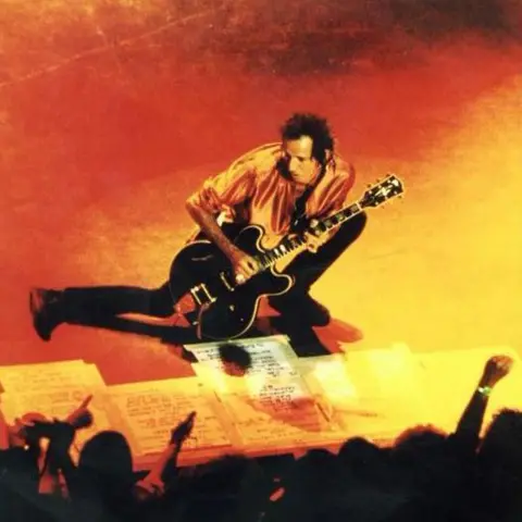 Keith Richards crouches on the stage while playing his guitar in a silk shirt, during a show at the Shepherd's Bush Empire in 1999