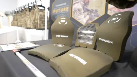 Curved and flat ballistic plates are displayed on a table next to each other for comparison.