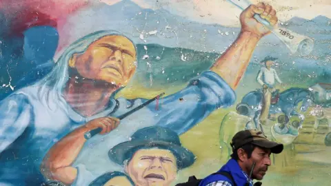 Getty Images An indigenous man walks next to a mural on October 30, 2019, during a meeting following the recent murder of an indigenous leader and four guards by suspected rebels, close to a checkpoint in Tacueyo, in the rural area of Toribio, department of Cauca, Colombia.