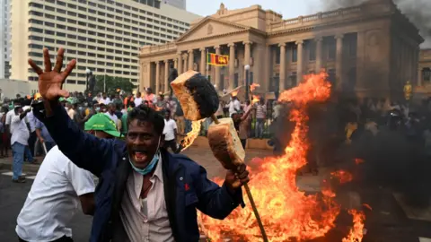 Getty Images A man with bread loafs on a stave protests with others outside the president's office in Colombo