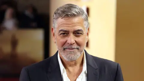 A man with greying hair and beard in a white shirt and black jacket smiles into the camera.
