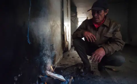 BBC/SHIRAAZ MOHAMED Derrick Brown crouches over trying to get a fire started to make coffee for himself and a friend in the derelict San Jose building in Johannesburg, South Africa