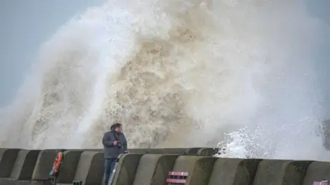 Getty Images People view the waves created by high winds and spring tides hitting the sea wall at New Brighton promenade on February 17, 2022 in Liverpool, England