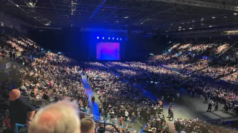 PA Media A full stadium of people wait for the main performer to arrive on a fluorescent stage.