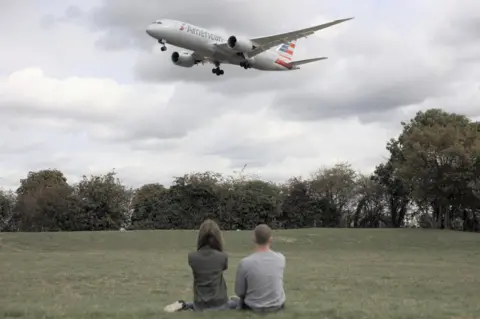 Bertie Taylor Two people in a park watch American Airlines flight land