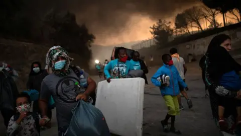 Reuters Refugees and migrants carrying their belongings flee a fire burning at the Moria camp on the island of Lesbos, Greece, 9 September 2020