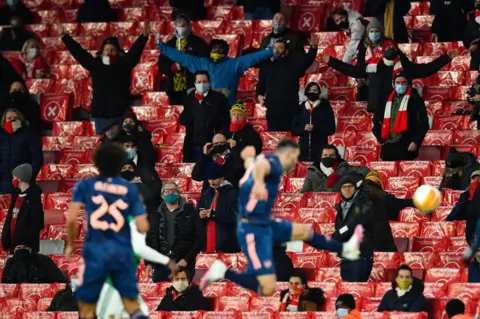 Reuters Socially-distanced football fans watch Arsenal in action at the Emirates Stadium