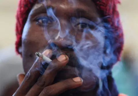 PHILIMON BULAWAYO/REUTERS A man smokes tobacco at the opening of the marketing season at the Tobacco Sales Floor in Harare.